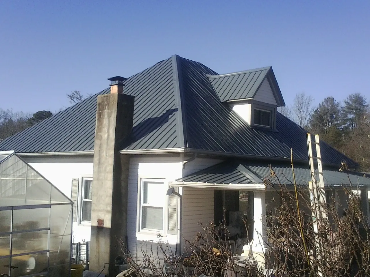 Dark blue standing seam metal roof on a white farmhouse with dormer — Slate & Tile Roof Repair by Roofing Brothers in Brewton