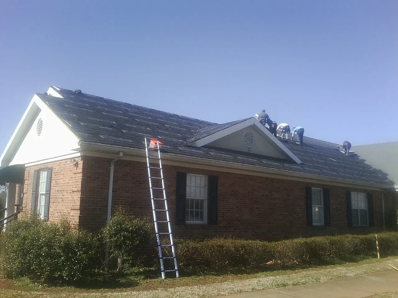 Crew tearing shingles off a brick ranch roof with a ladder set — Metal Roof Repair work by our crew in Brewton