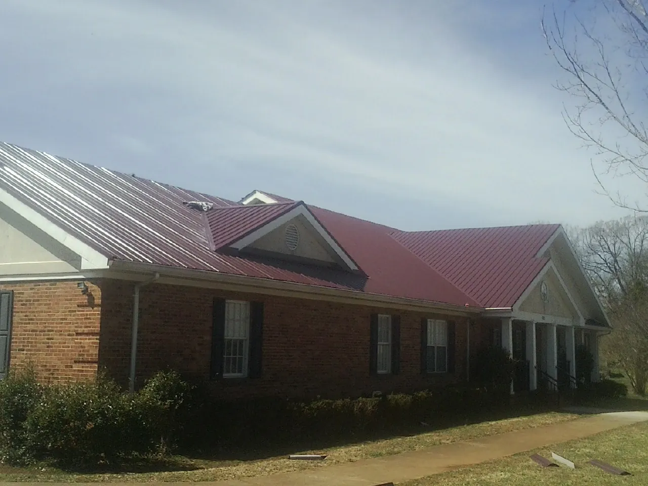 Red metal roof with gabled entries on a long brick building, from a Hail Damage Roof Repair job in Brewton