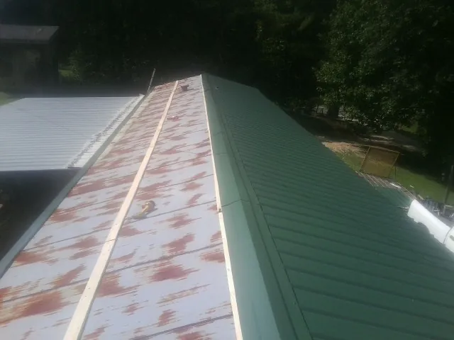 Old rusted panels beside newly installed green metal roofing — Wind Damage Roof Repair by Roofing Brothers in Brewton