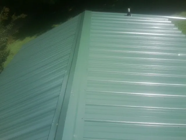 New green metal panels meeting at the ridge of a roof — Flat Roof Repair work by our crew in Brewton