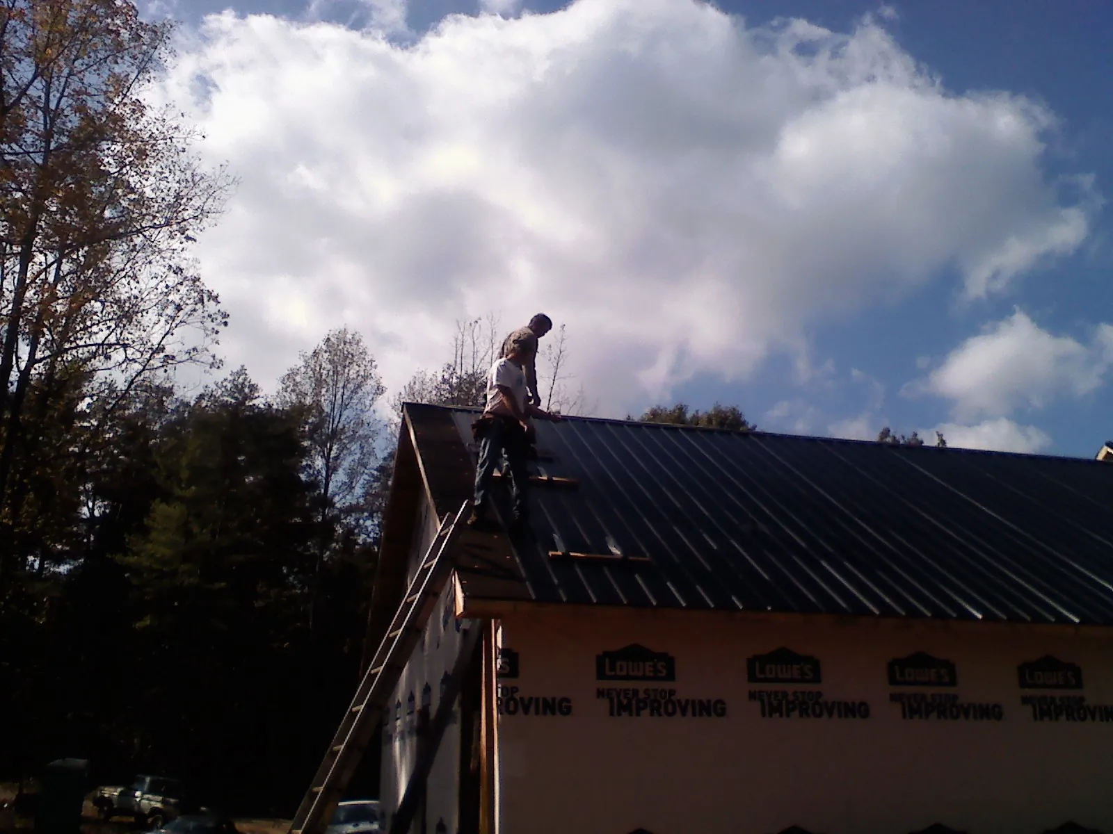 Roofer fastening dark metal panels high against a cloudy sky, from a Roof Inspection job in Brewton
