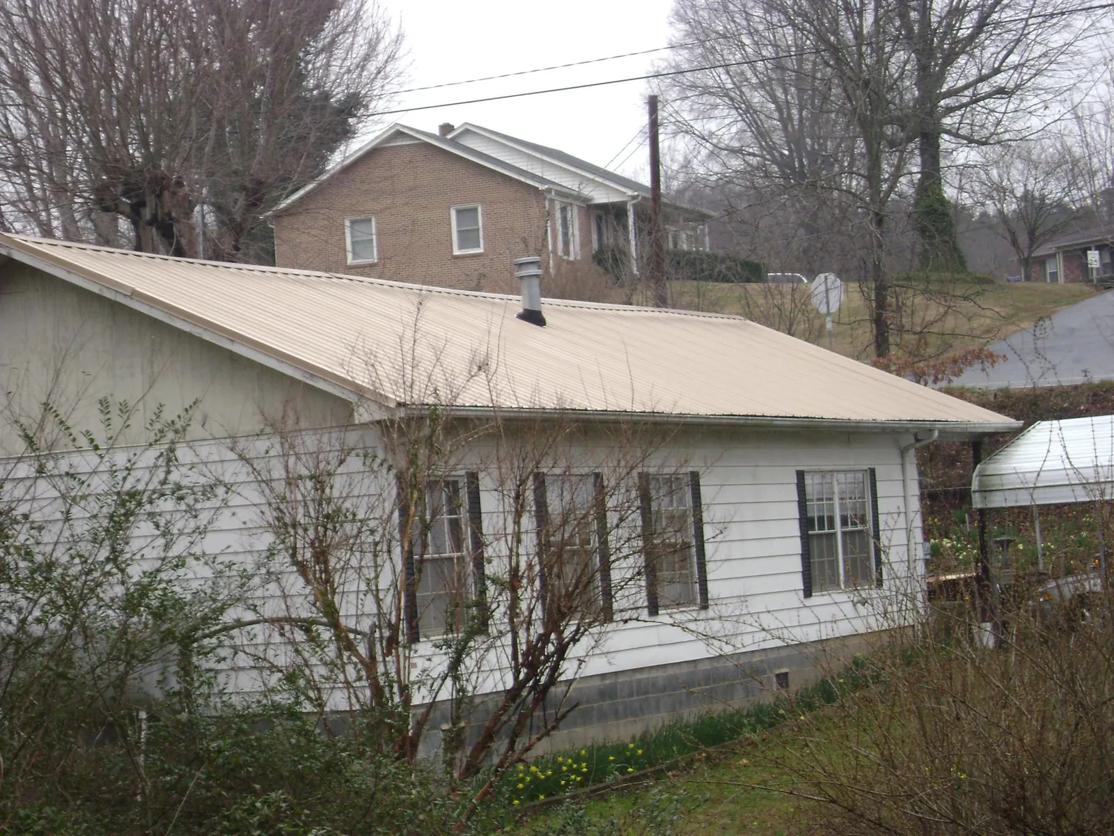Tan metal roof on a white sided house set into a hillside — Commercial Roofing by Roofing Brothers in Brewton