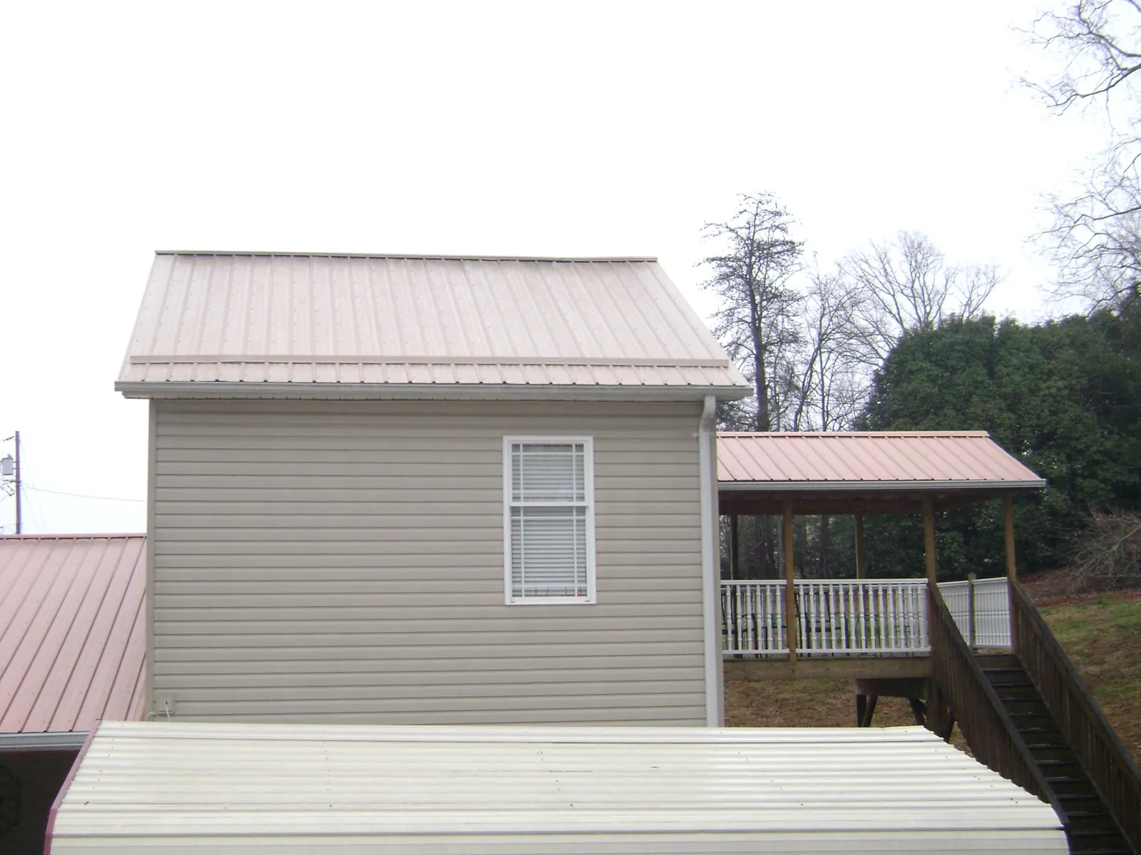 Tan metal roofs on a two story addition and attached porch, from a Roof Replacement job in Brewton